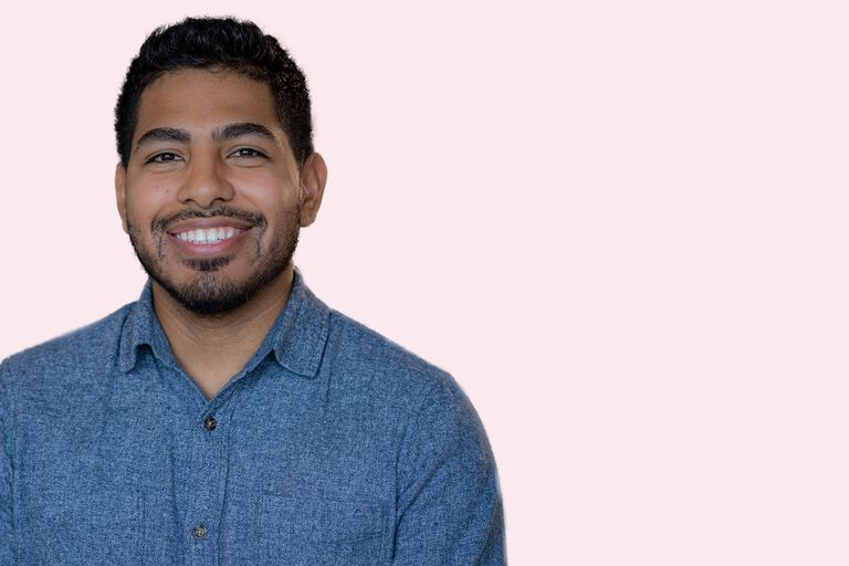 Person wearing a blue button-up shirt against a light pink background