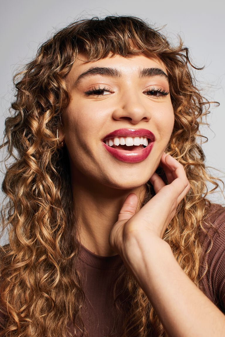 Close-up of smiling model with curly hair wearing the Glass Lips look