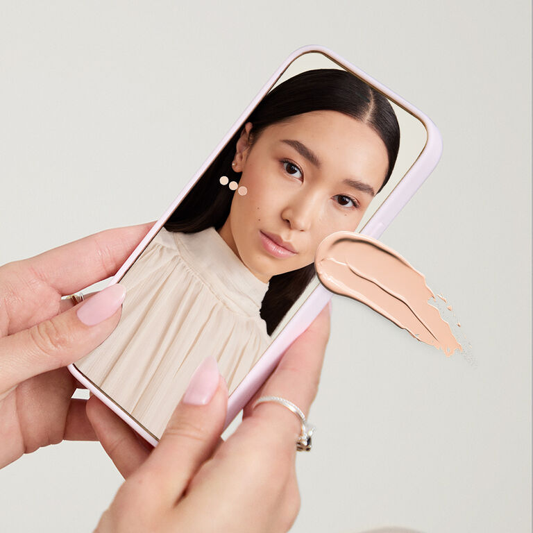 Hands holding a mobile device showing the Mary Kay Foundation Finder