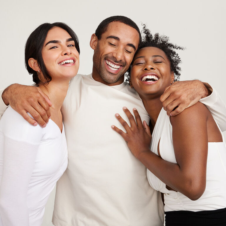 A group of two women and one man laughing and hugging each other