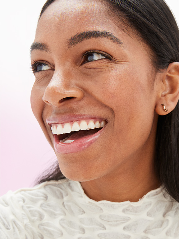 A woman with dark hair and dark skin smiles and looks away from the camera.